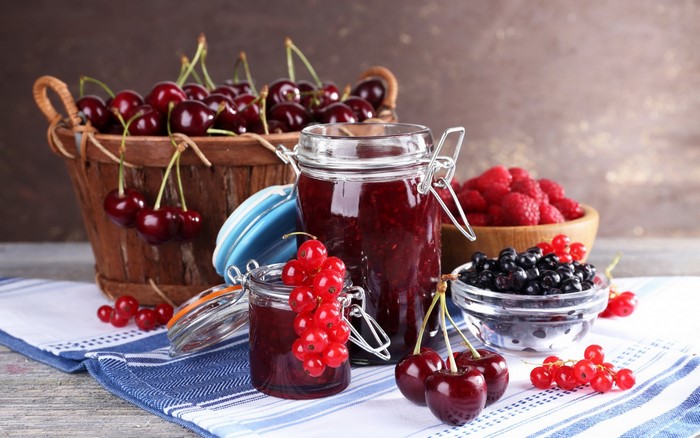 Jars of berry jam with fresh cherries, raspberries, and currants