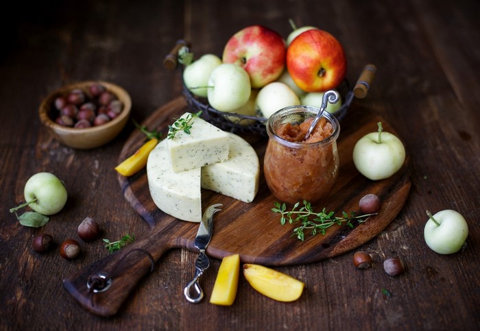 Cheese, apples, jam, and nuts on a wooden board