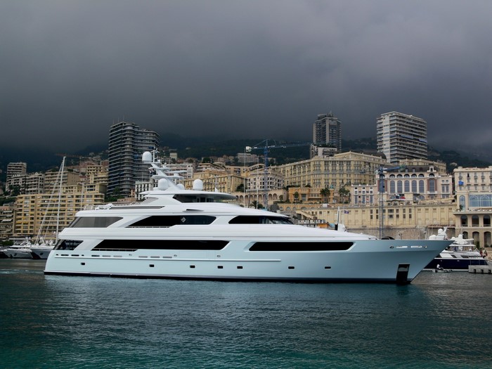 White yacht docked in a harbor with city buildings in the background
