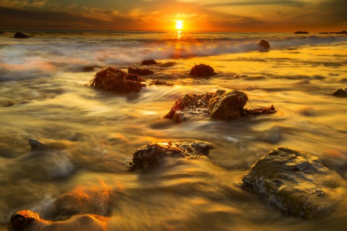 Sunset over the ocean with rocks and waves