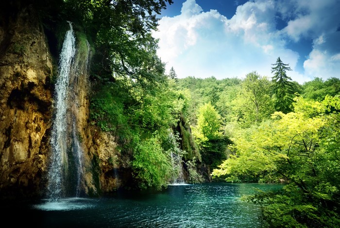 Waterfall cascading into a turquoise lake surrounded by a lush green forest