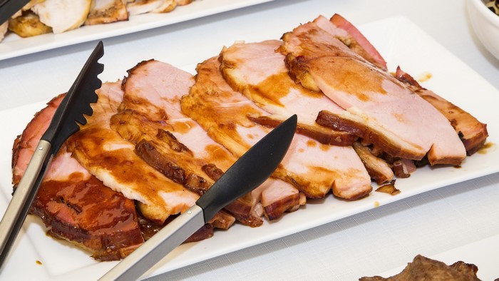 Sliced glazed ham on a platter with tongs