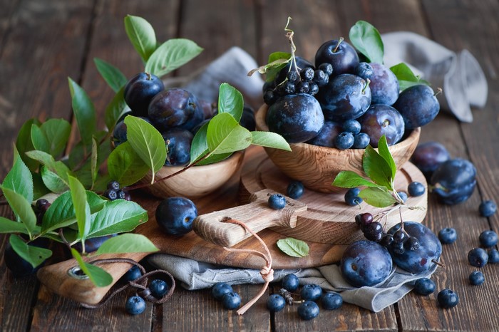 Plums and blueberries in wooden bowls on a rustic table