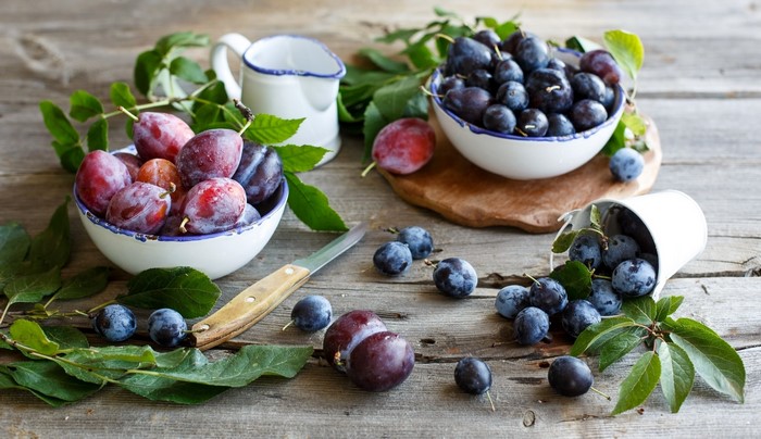 Plums in bowls with leaves and a knife