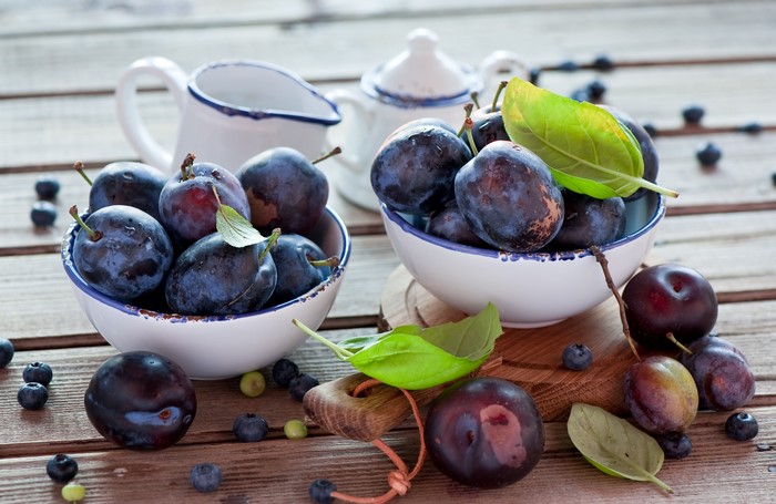 Plums and blueberries in bowls on a wooden table