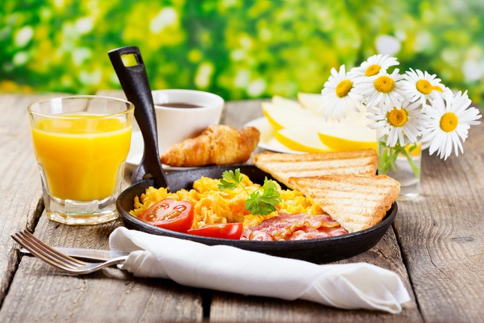 Breakfast with scrambled eggs, bacon, toast, juice, and coffee