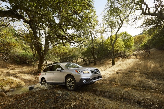 Silver Subaru Outback driving through a stream in a forest