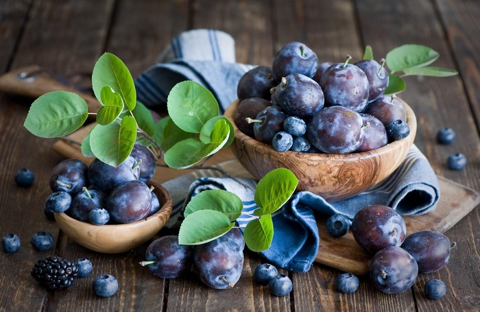 Plums and blueberries in wooden bowls on a rustic table