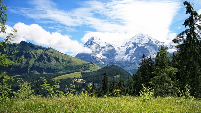 Snow-capped mountains and green hills under a cloudy sky