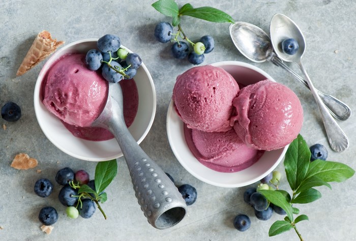 Blueberry ice cream in bowls with fresh blueberries and spoons