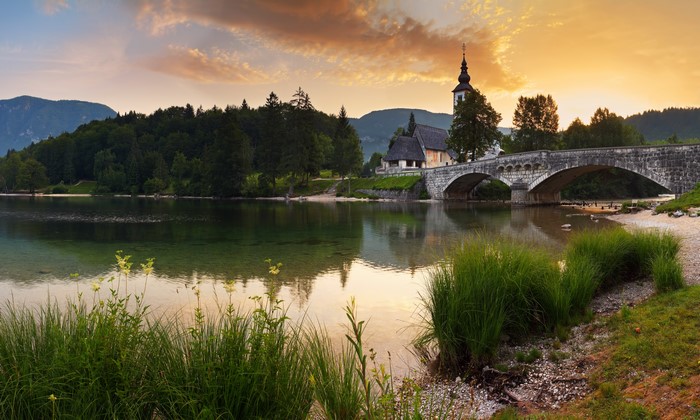 Stone bridge and church by a lake at sunset