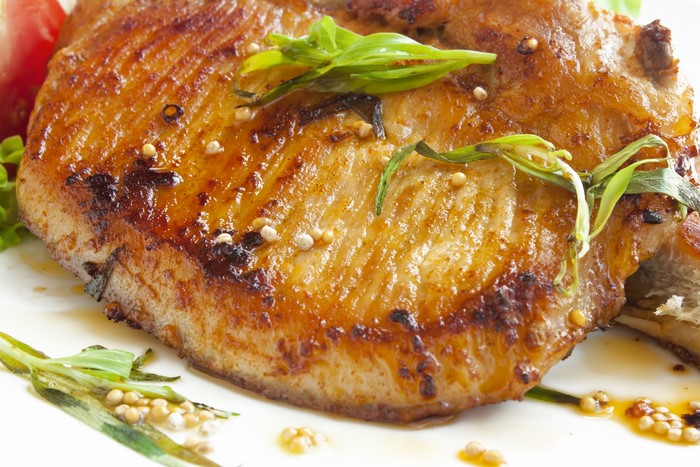 Close-up of a grilled pork chop with herbs and mustard seeds