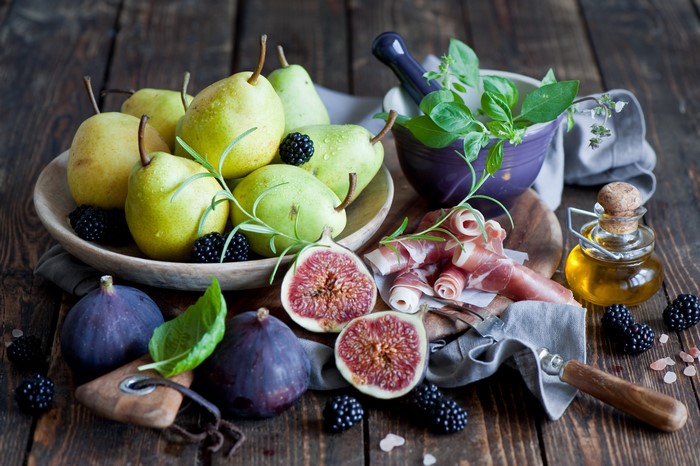Pears, figs, blackberries, prosciutto, and olive oil on a wooden table