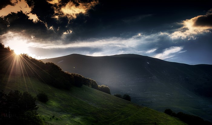 Sun rays over mountains and green hills in Italy