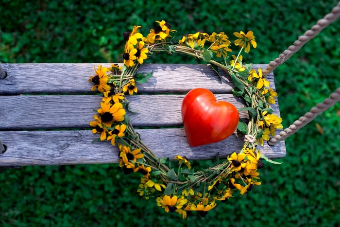 Heart-shaped flower wreath and red heart on a bench