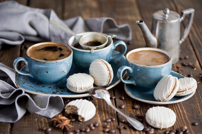 Two cups of coffee with macarons and a teapot