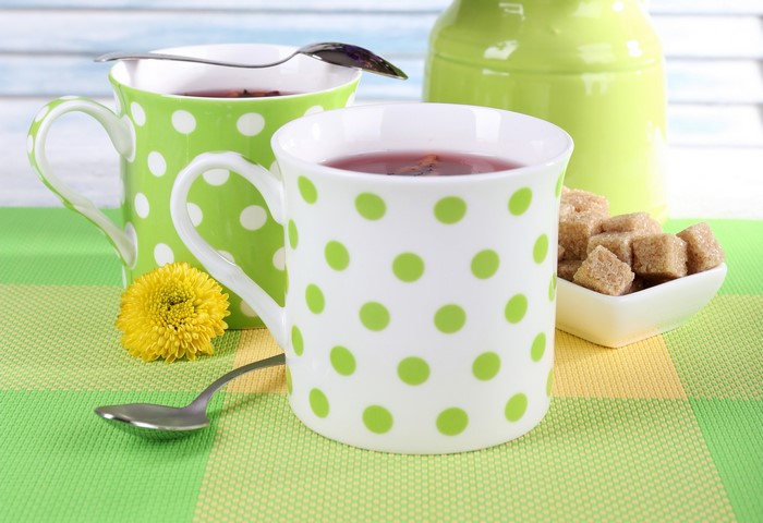 Two polka dot mugs of tea with sugar cubes and a flower