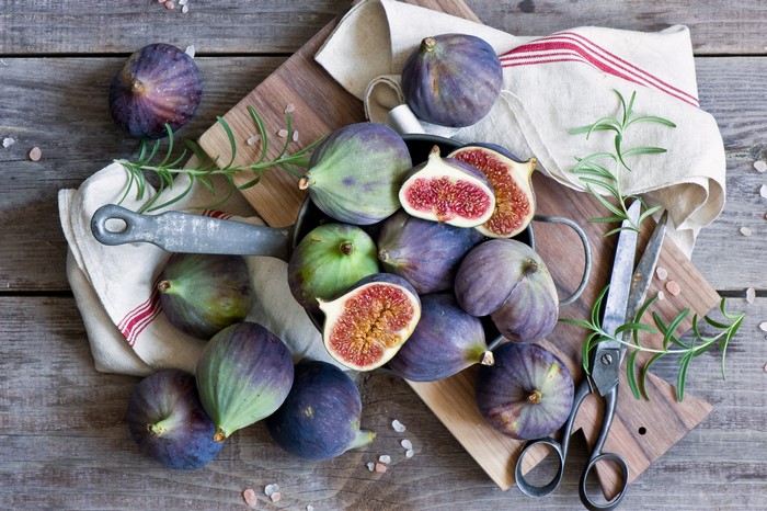 Fresh figs on a wooden table with rosemary and scissors
