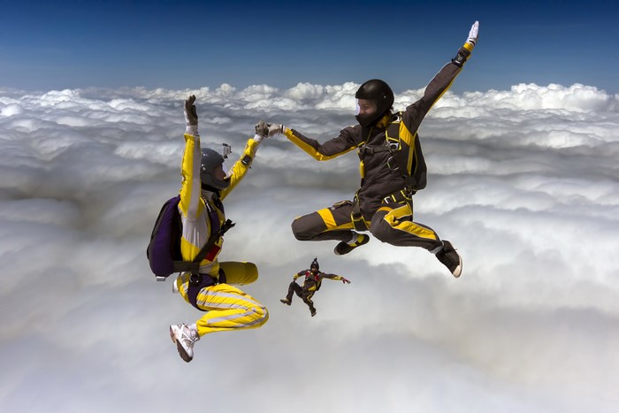 Three skydivers in formation above clouds