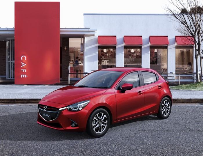 Red 2014 Mazda Demio parked outside a cafe