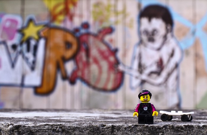 Lego figure with skateboard in front of graffiti wall
