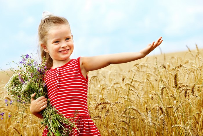 Girl in red dress holding flowers in a wheat field