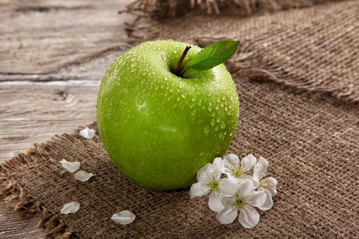 Green apple with water droplets and flowers