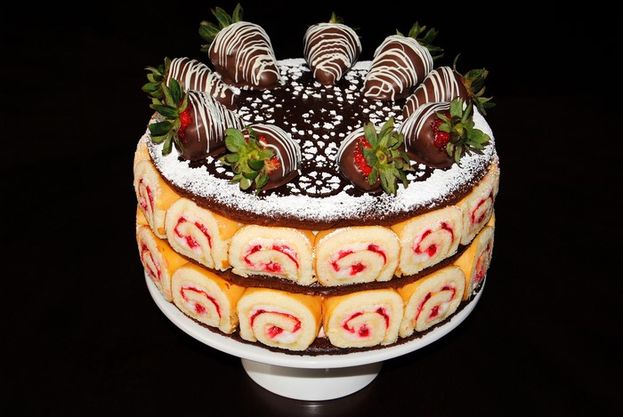 Two-tiered cake with Swiss rolls and chocolate-covered strawberries