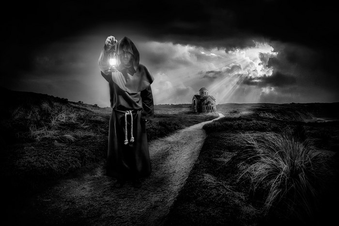 Monk with lantern on path to church under stormy sky