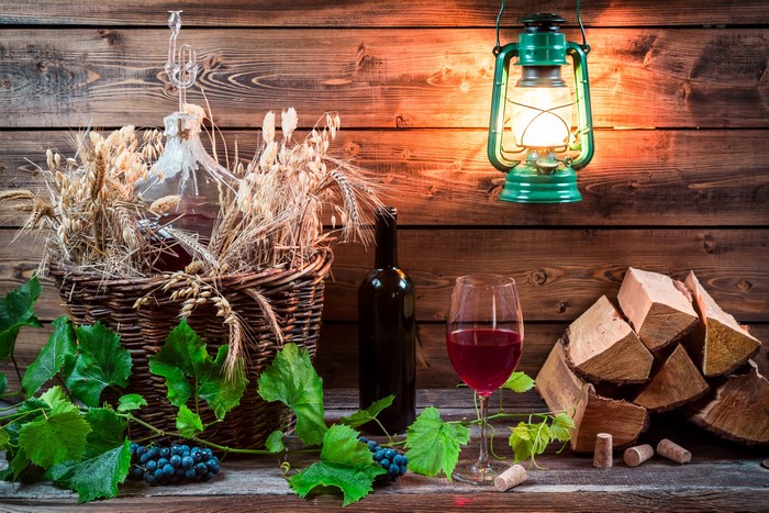 Still-life of wine, grapes, and wheat in a wicker basket with a kerosene lamp