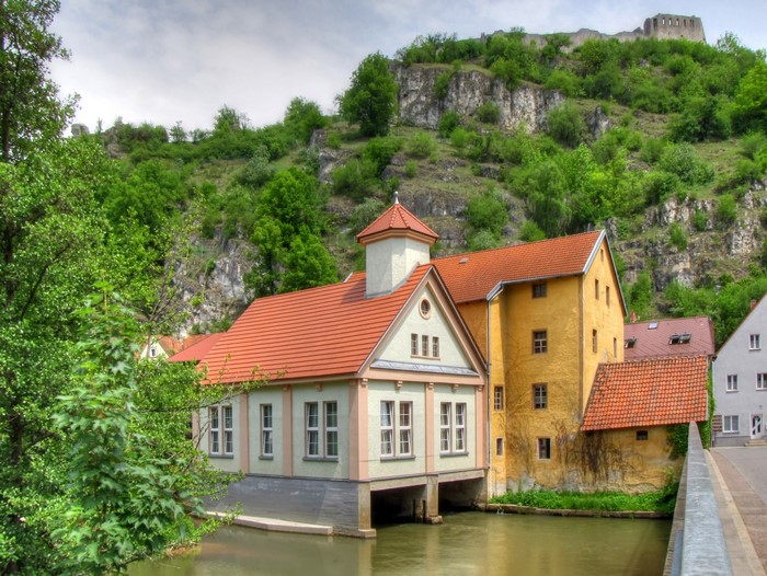 Houses on a river in Germany with castle ruins on a hill
