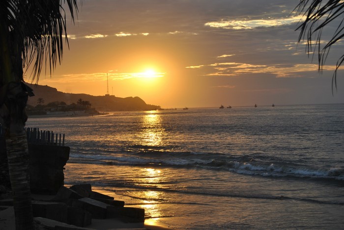 Sunset over the sea with boats and a hill