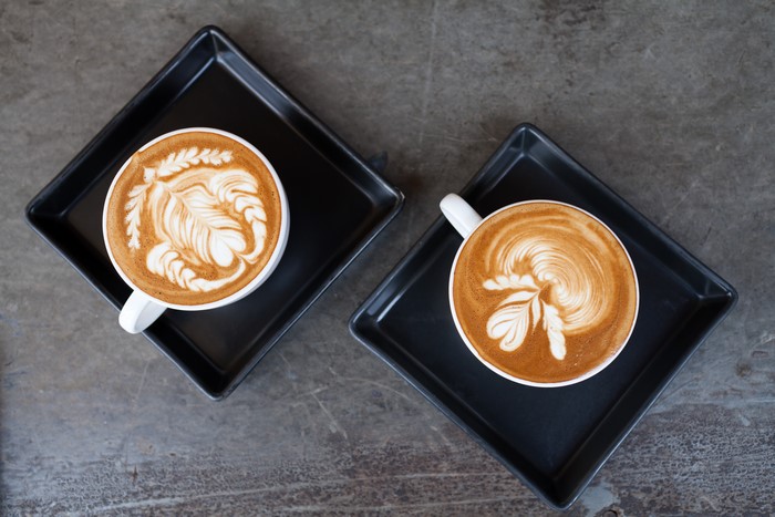 Two cups of latte art coffee on black square plates