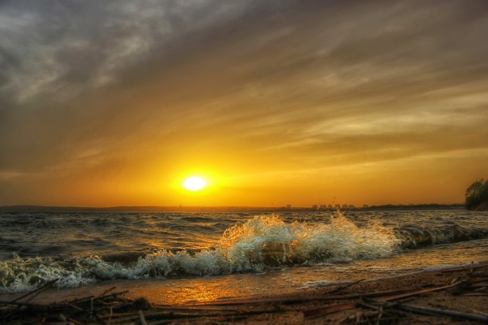Sunset over the ocean with waves crashing on the shore