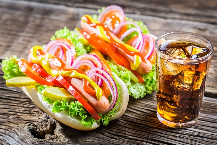 Two hot dogs with toppings and a glass of cola