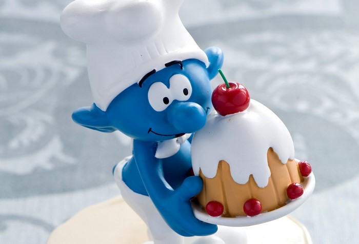 Chef Smurf holding a cake with cherries
