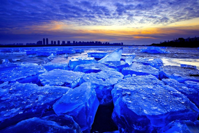 Ice floes on a river at sunset with city skyline