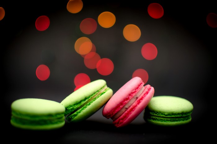 Four colorful macarons on a dark background with bokeh lights