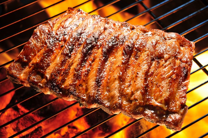 Rack of ribs cooking on a grill over flames