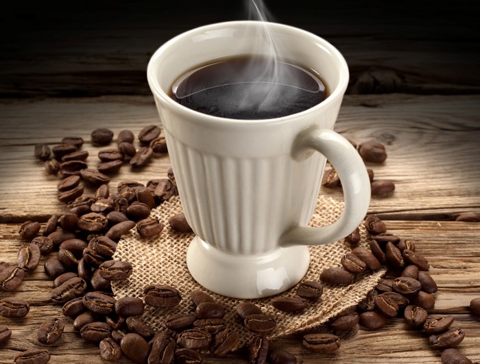 Hot coffee in a white cup with coffee beans