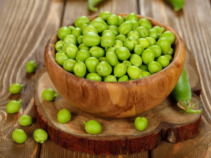 Bowl of fresh green peas on a wooden table