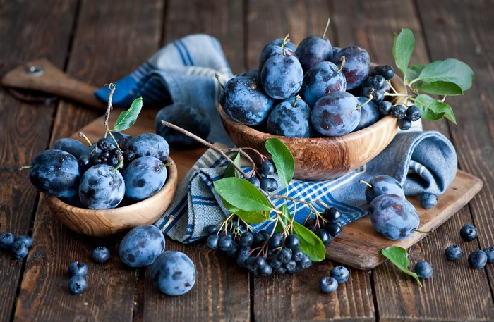 Plums and Aronia berries in wooden bowls