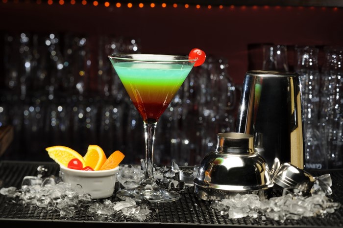 Layered cocktail with orange garnish and cocktail shaker