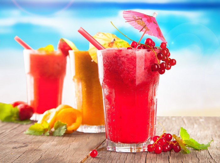 Four colorful fruit juices with garnishes on a wooden table