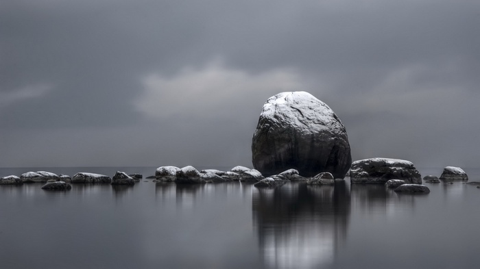 Snow-covered rocks in calm water under cloudy sky