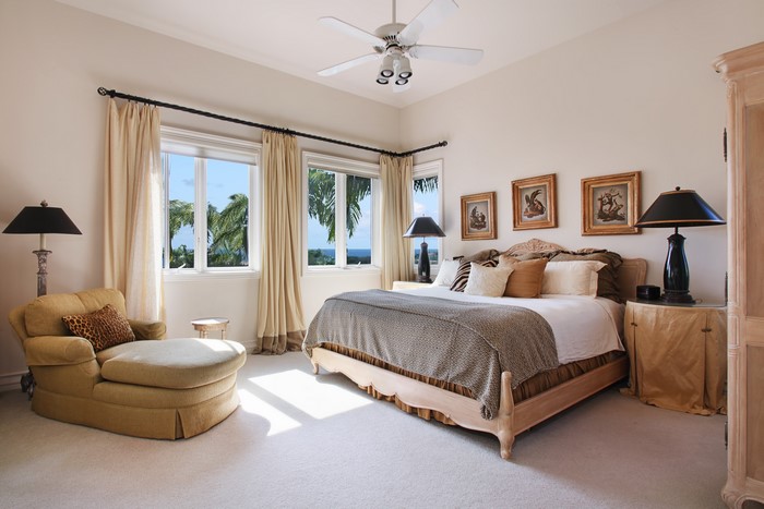 Bedroom with armchair, bed, and windows overlooking palm trees