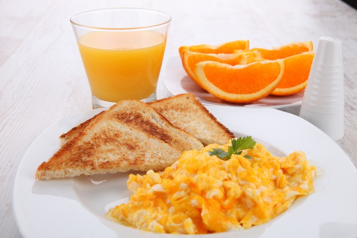 Scrambled eggs with toast, orange juice, and orange slices