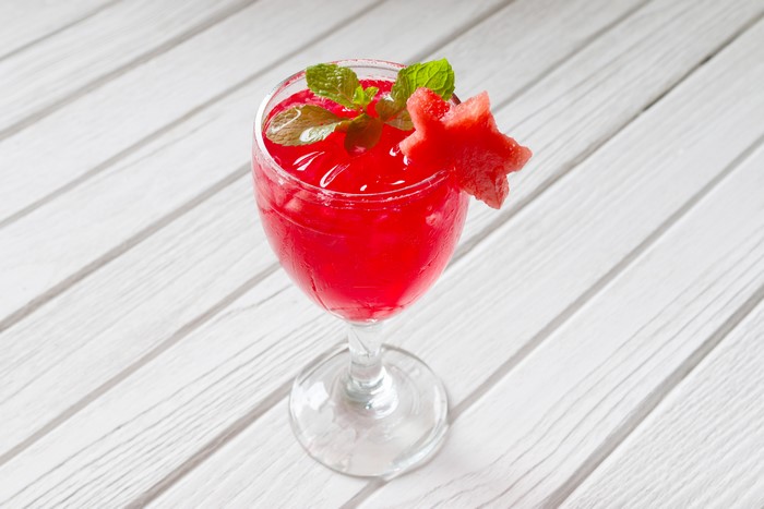 Red drink in a stemmed glass with watermelon garnish