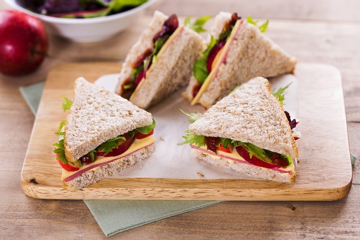 Four triangular sandwiches with cheese and salad on a wooden board