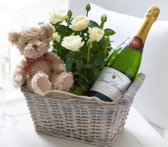 Teddy bear, white roses, and champagne in a wicker basket